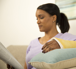 Woman reading while propping up arm in cast on pillows.