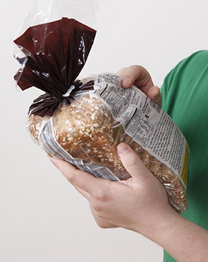 Closeup of person's hands holding bag of bread, pointing at nutrition label.