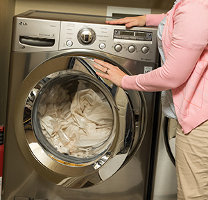 Person loading sheets into home washing machine.