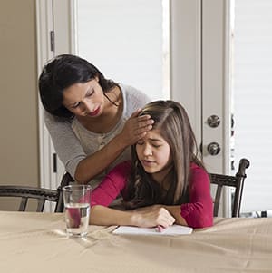 Teen doing homework, adult feeling their forehead.