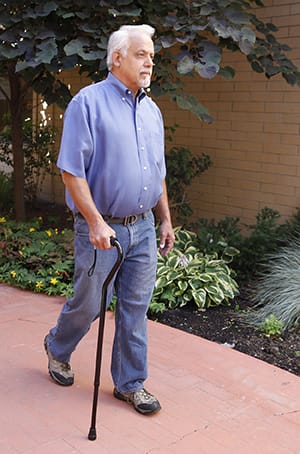 Person walking outdoors using a cane.